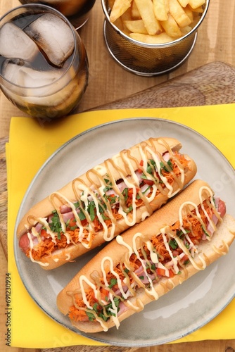 Delicious hot dogs with bacon, carrot and parsley served on wooden table, flat lay