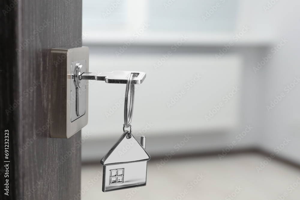 Mortgage and real estate. Open door with key and house shaped keychain against blurred background, space for text Mortgage and real estate. Open door with key and house shaped keychain against blurred background, space for text