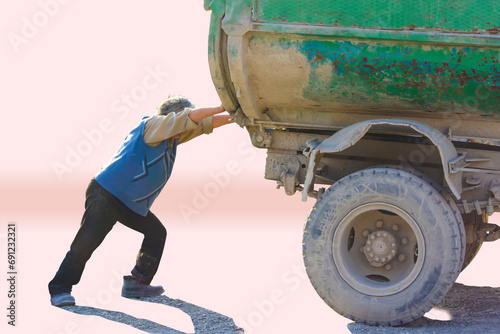 A man pushing an old dump truck from behind.