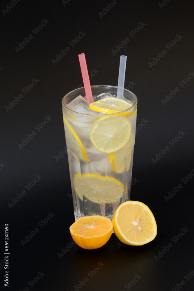 A tall glass of refreshing lemonade with ice and citrus pieces on a black background. A tall glass of refreshing lemonade with ice and citrus pieces on a black background.