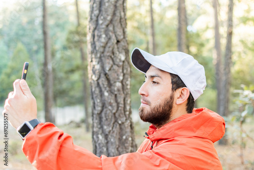 Hombre joven con barba tomando una selfie en el bosque.