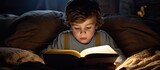 Front view of a child of European descent reading a book in bed at night with some empty space to the side.