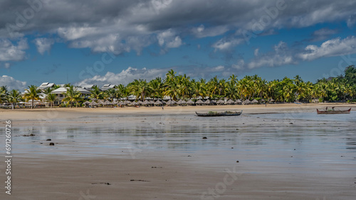 Low tide in the ocean. Wooden boats with fishing nets and fishermens are moored in shallow water. In the distance, on the sandy shore, you can see the villas of the hotel, a row of straw sun umbrellas photo