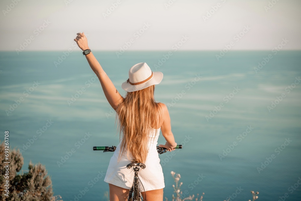 Naklejka premium A woman cyclist on a mountain bike looking at the landscape sea. Adventure travel on bike.