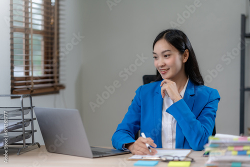 Young Asian business woman sitting working in modern office. Asia business woman sitting smiling and happy with laptop computer in the office.