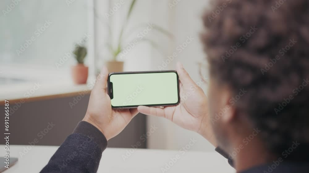 Young black man is watching on horizontal phone screen and nodding, office set up. Young black man is watching on horizontal phone screen and nodding, office set up.