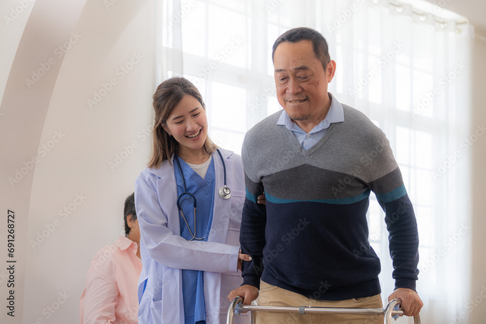 Obraz premium Asian young nurse support senior older man walk with walker. Beautiful nurse help and take care. elderly mature grandpa patient doing physical therapy with a group of senior friends in hospital.