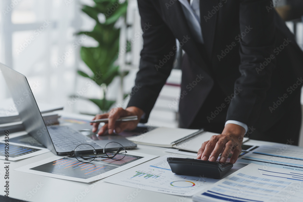 Asian businesswoman works on laptop and calculates with financial calculator from graphs, statistics, charts. Planning. Business success results in modern office. Asian businesswoman works on laptop and calculates with financial calculator from graphs, statistics, charts. Planning. Business success results in modern office.