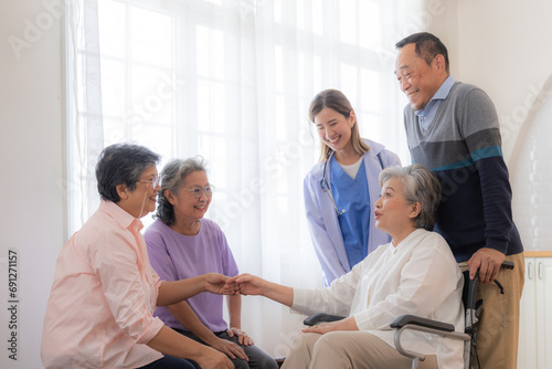 Asian young nurse support couple senior older man and woman in a wheelchair. elderly mature and a group of senior friends living in the hospital. socializing of retired people.