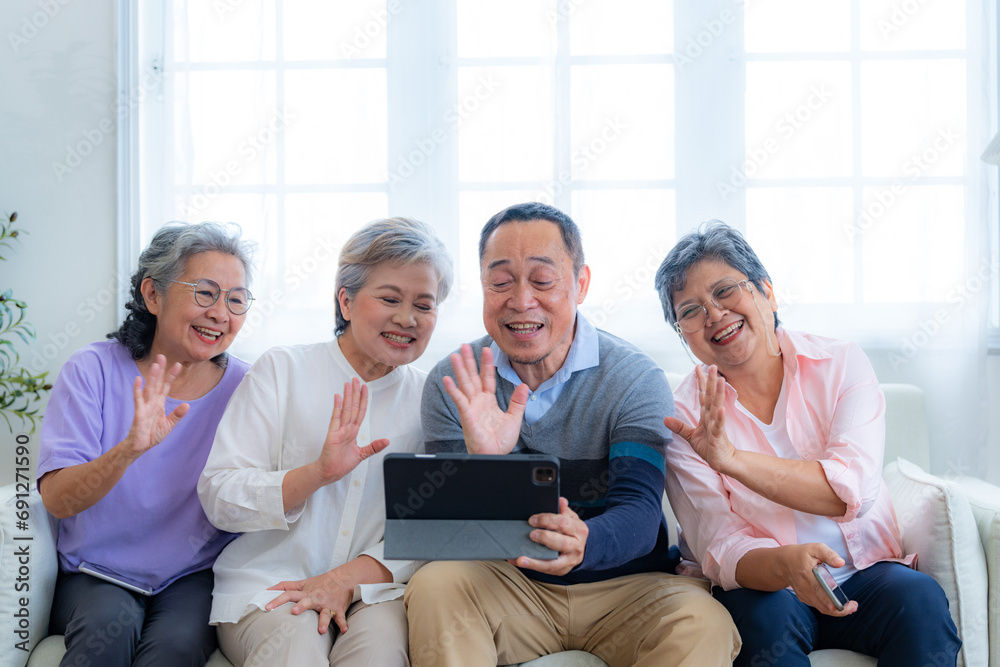 Fototapeta premium Happiness of the group females and male elderly talking with Video Call from smart tablet. Senior people are talking and enjoy together at the living room. Joyful retired friends enjoying relaxation.