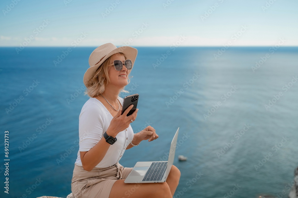 Freelance women sea working on the computer. Good looking middle aged woman typing on a laptop keyboard outdoors with a beautiful sea view. The concept of remote work.