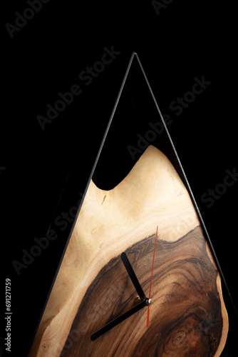 Wooden triangular wall clock on dark grey background. Luxurious accessories for home, office or restaurant made of wood and epoxy in loft style. Business style background.