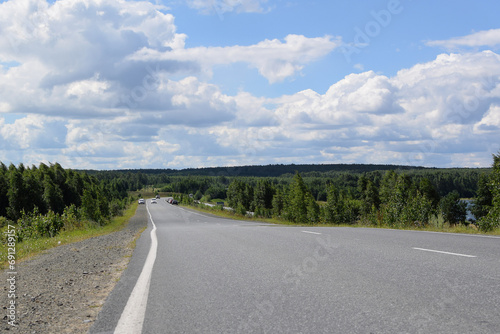 Cars on the highway. Dense forest along the road. Beautiful summer landscape, white clouds on a blue sky.