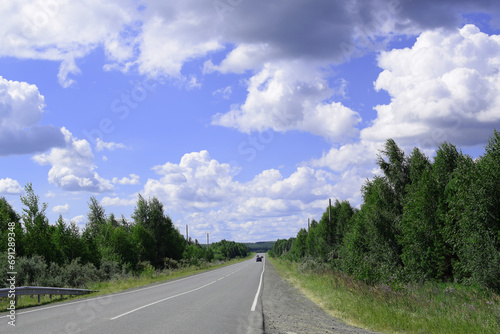 Cars on the highway. Road along the forest. Beautiful summer landscape, white clouds on a blue sky.