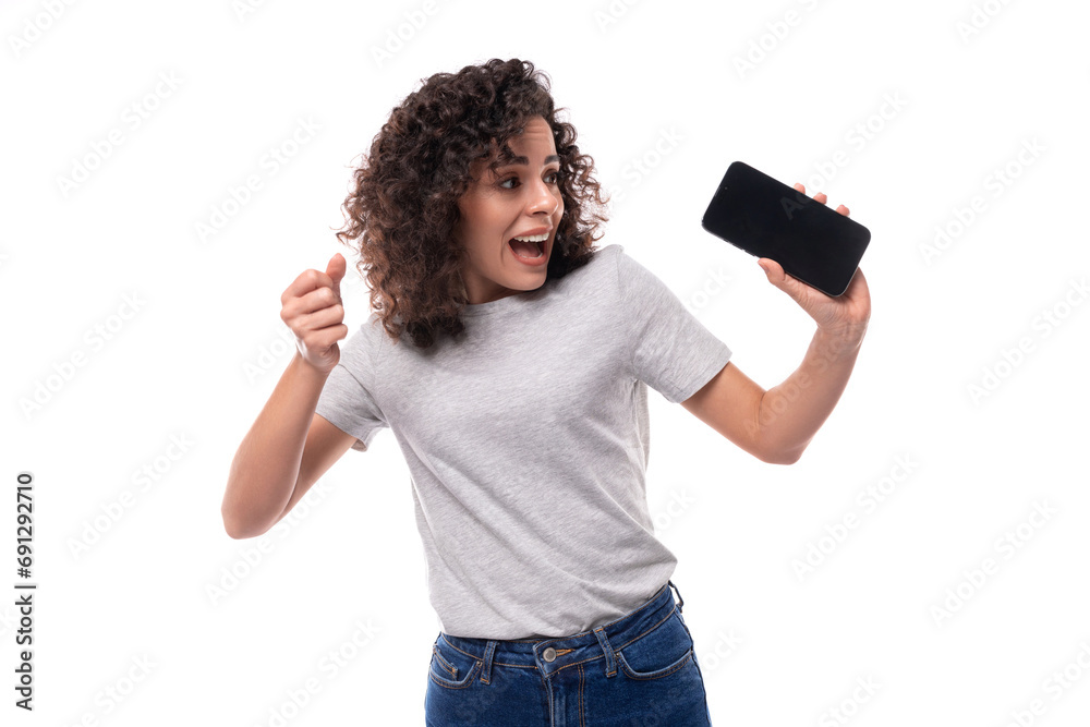 young slender 30 year old caucasian woman with curly hair in a gray t-shirt shows the screen of a smartphone with a mockup for advertising young slender 30 year old caucasian woman with curly hair in a gray t-shirt shows the screen of a smartphone with a mockup for advertising