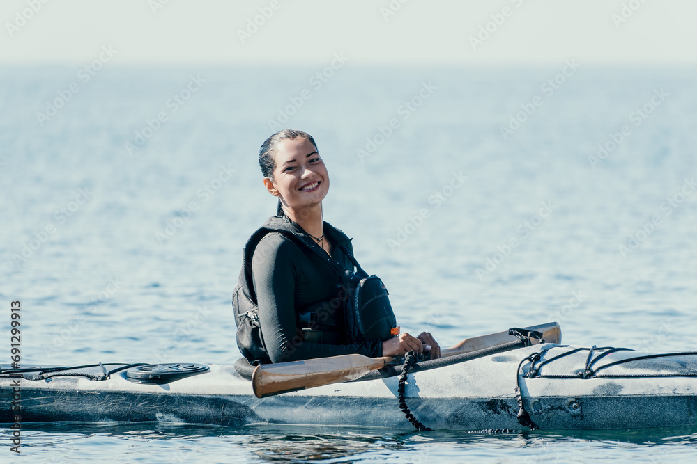 Obraz premium Woman sea kayak. Happy smiling woman in kayak on ocean, paddling with wooden oar. Calm sea water and horizon in background. Active lifestyle at sea. Summer vacation.