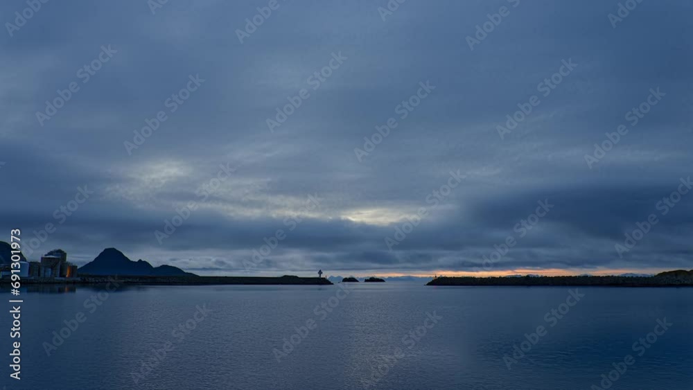 View towards the sea in early morning. A fish oil factory behind protective breakwater and a fishing boat leaving harbor. Lofoten, Northern Norway. View towards the sea in early morning. A fish oil factory behind protective breakwater and a fishing boat leaving harbor. Lofoten, Northern Norway.