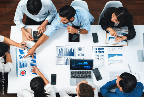 Top view analyst team utilizing BI Fintech to analyze financial data at table in meeting room. Analytic BI dashboard power on paper for business insight and strategic marketing planning. Prudent