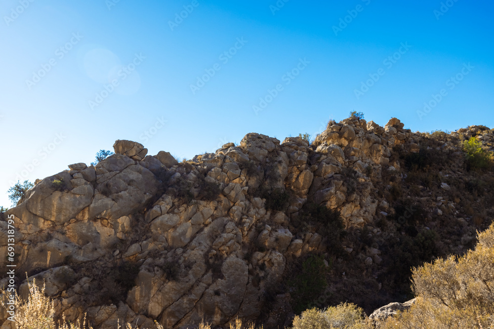 Rock, close up isolated photo of rich golden geometric mountain wall against blue sky for abstract