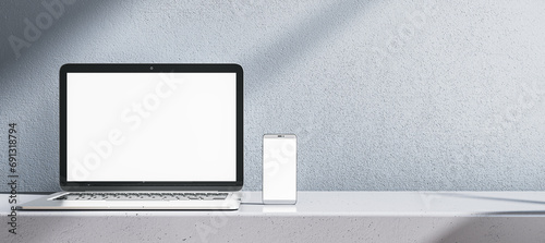 Close up of empty white laptop computer and smartphone on gray desk. Concrete wall background. Device presentation and online education concept. Mock up, 3D Rendering.