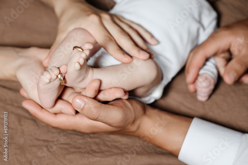 Mom and dad hold the legs of their child, gold wedding rings on the toes.