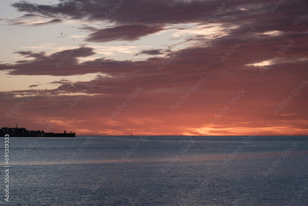 Playa de Málaga, amanecer sobre el mar, primeros rayos de sol, al fondo vista del puerto