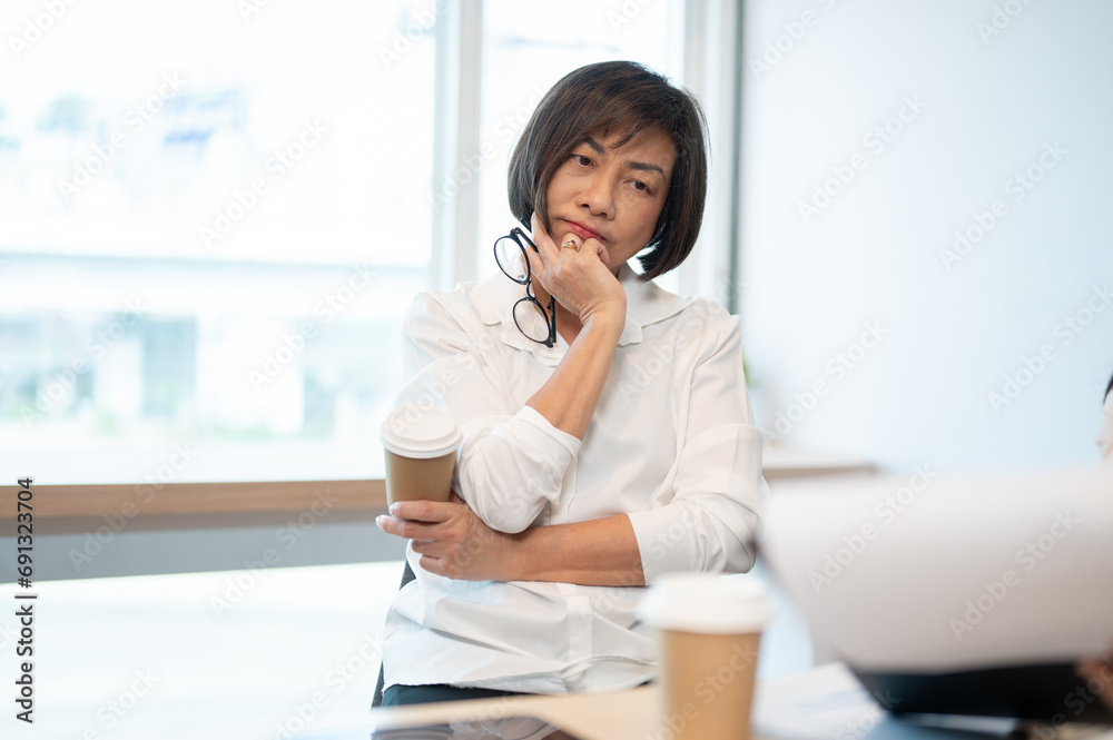 A thoughtful senior Asian female boss is in the meeting, listening to her employee's presentation. A thoughtful senior Asian female boss is in the meeting, listening to her employee's presentation.