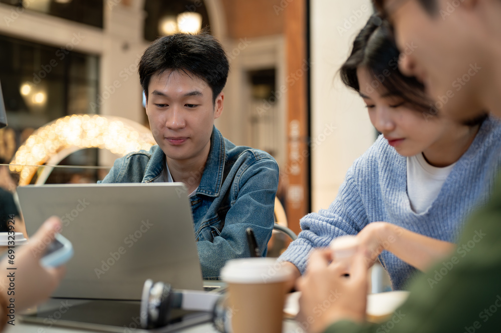 Fototapeta premium Group of young Asian college students is working on a co-project while sitting in a cafe together.