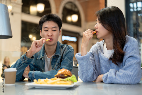 Happy young Asian couple enjoying eating fries, dating, and having lunch at a restaurant together.