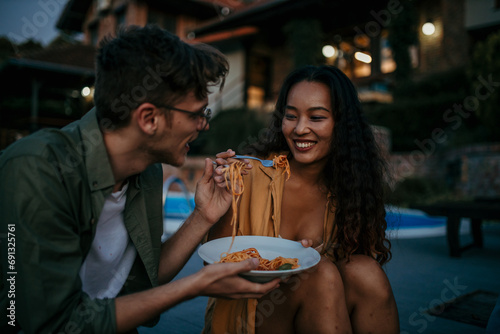 A multiethnic couple share pasta and laughter outdoors