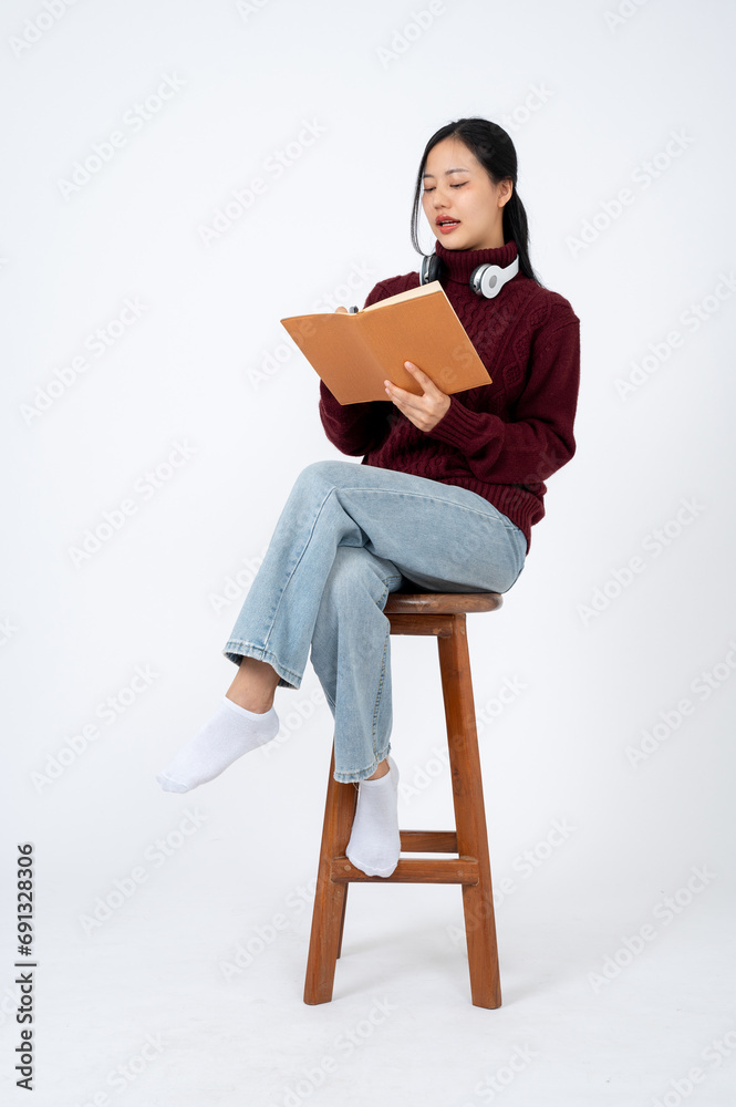 Beautiful Asian woman in a sweater is writing her diary on a chair on an isolated white background. Beautiful Asian woman in a sweater is writing her diary on a chair on an isolated white background.