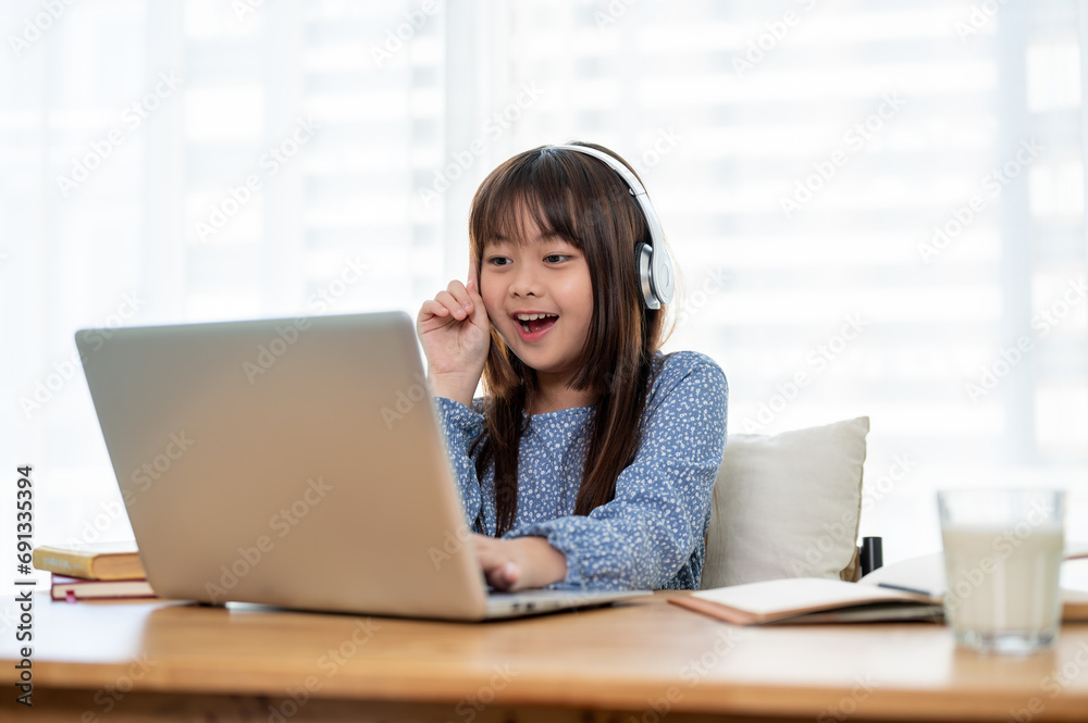 A happy young Asian girl is enjoying studying online on her laptop at home. A happy young Asian girl is enjoying studying online on her laptop at home.