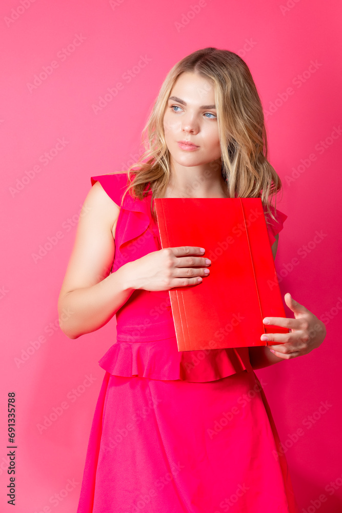 Thoughtful Winsome Smiling Caucasian Girl in Red Summer Dress With Colorful Red Folder Against Coral Background. Thoughtful Winsome Smiling Caucasian Girl in Red Summer Dress With Colorful Red Folder Against Coral Background.