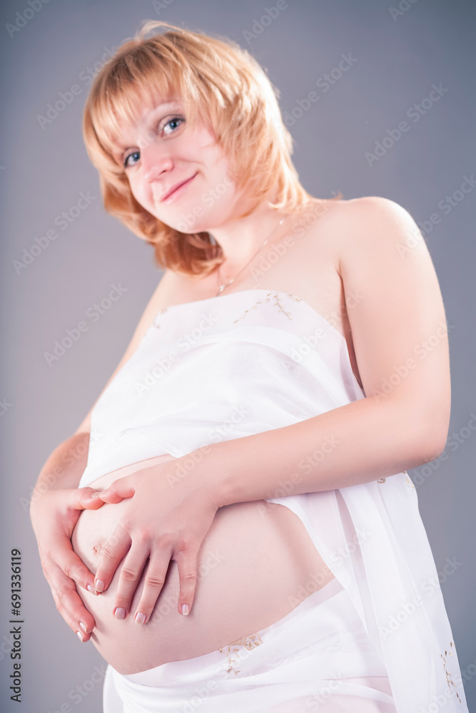 Blond Pregnant Woman Touching Belly With White Veil As Middle Aged Mother Caressing Tummy As Healthy Pregnancy Concept On Gray Background. Blond Pregnant Woman Touching Belly With White Veil As Middle Aged Mother Caressing Tummy As Healthy Pregnancy Concept On Gray Background.