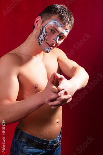 Smiling Masculine Caucasian Brunette Man Painted With Unique Face Art Painting Posing With Connected Hands Against Red Background.