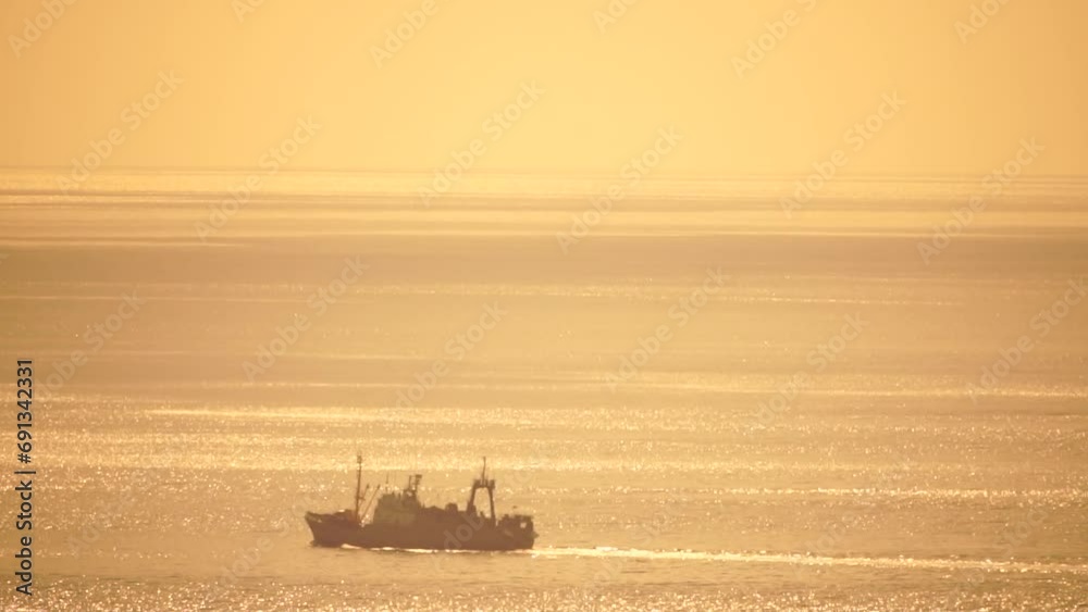 Fishing ship trawler at sunset in the sea. Abstract aerial sea summer ocean sunset nature background. Small waves on calm water surface in motion blur with golden bokeh lights from sun. Fishing ship trawler at sunset in the sea. Abstract aerial sea summer ocean sunset nature background. Small waves on calm water surface in motion blur with golden bokeh lights from sun.