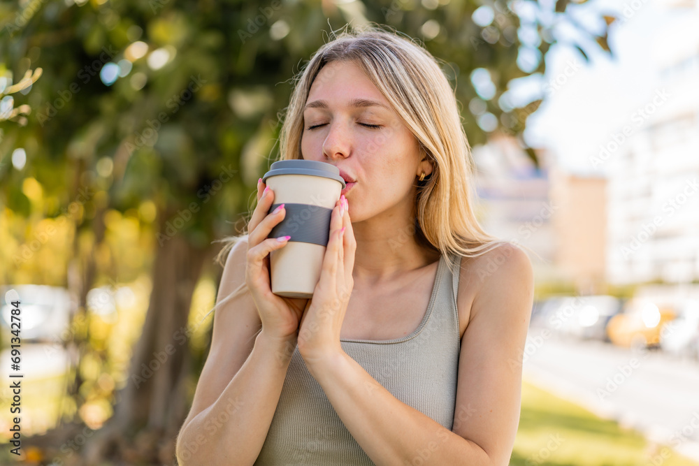Young blonde woman at outdoors holding a take away coffee