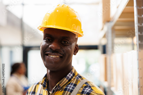 African american warehouse package handler in yellow helmet portrait. Industrial storehouse young loader wearing protective workwear smiling and looking at camera close up