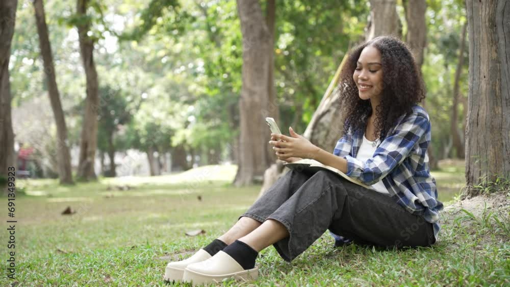 female university student Woman writing in notebook holding smartphone Sitting on the ground under a tree in the park Students are preparing for exams. female university student Woman writing in notebook holding smartphone Sitting on the ground under a tree in the park Students are preparing for exams.