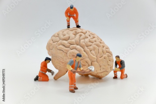 miniature figurines of men at work with a huge human brain isolated on a white background