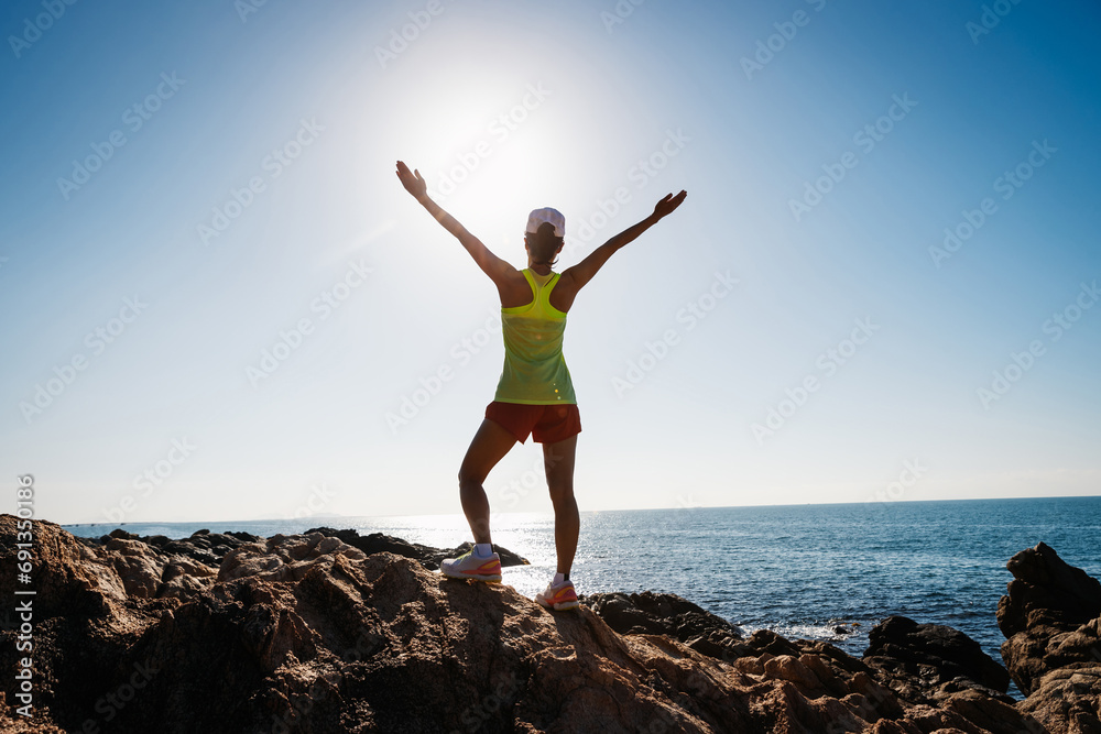 Woman open arms on sunrise seaside rocky mountains Woman open arms on sunrise seaside rocky mountains