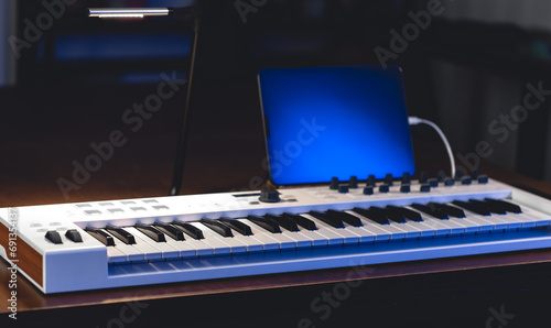 Musical keyboard and tablet in a dark room, music production.