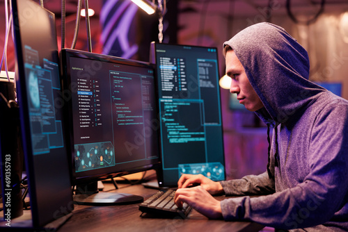 Asian criminal in hood hacking server and stealing data while committing online crime. Young hacker running illegal malicious software code on computer screen for cracking password photo