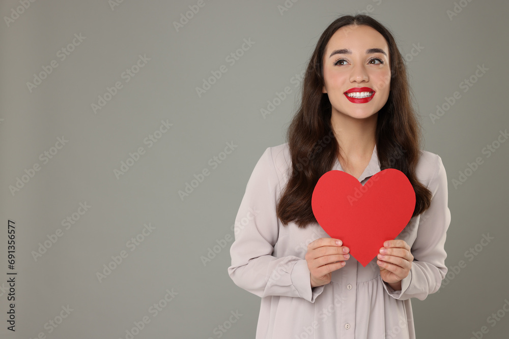 Beautiful young woman with paper heart on grey background, space for text Beautiful young woman with paper heart on grey background, space for text