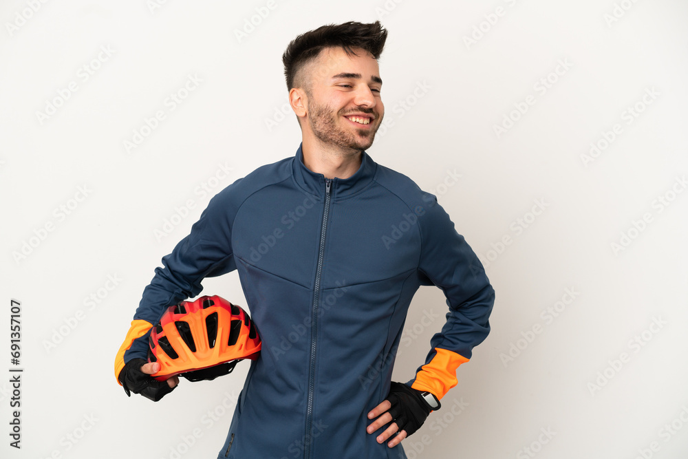 Young cyclist man isolated on white background posing with arms at hip and smiling - obrazy, fototapety, plakaty 