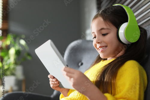 Cute little girl with headphones and tablet listening to audiobook at home photo