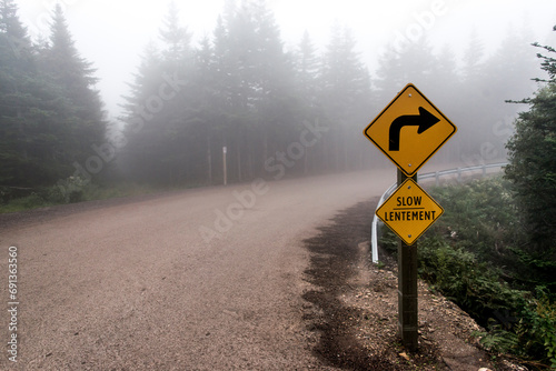 Slow Lentement sign Warning yellow roads signs road in Background foggy Cape Breton Island Nova Scotia Highlands Canada photo