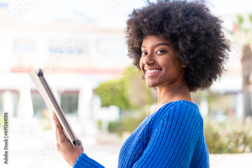 African American girl holding a tablet at outdoors smiling a lot