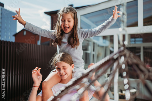 Smiling girl carrying sister on shoulders in front of house photo