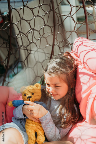 Smiling girl playing with stuffed toy in porch swing photo